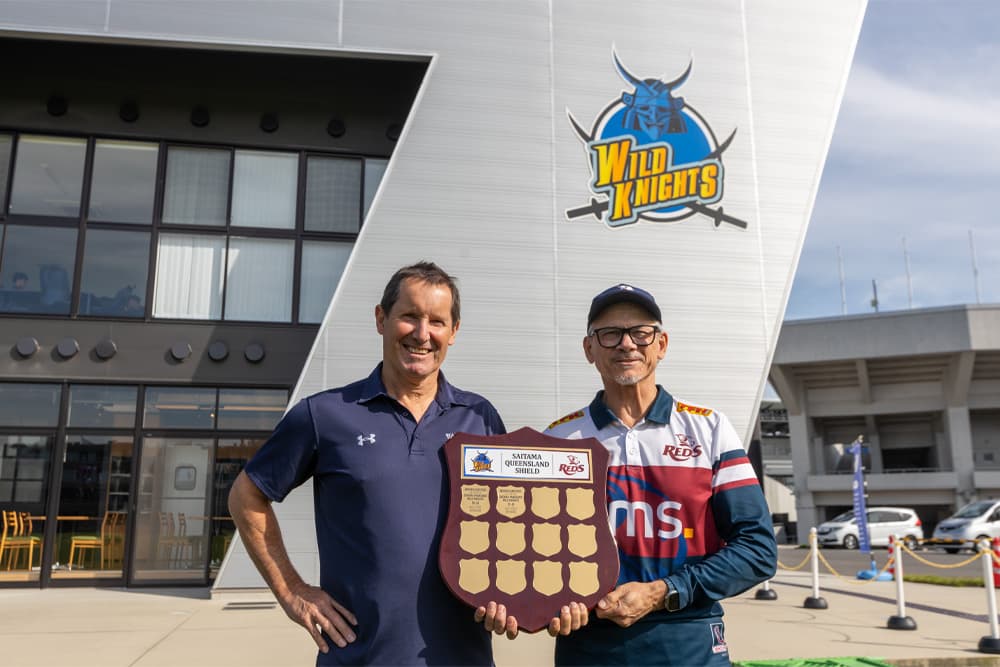 Wild Knights coach Robbie Deans and Reds coach Les Kiss display the Saitama-Queensland Shield in Kumagaya