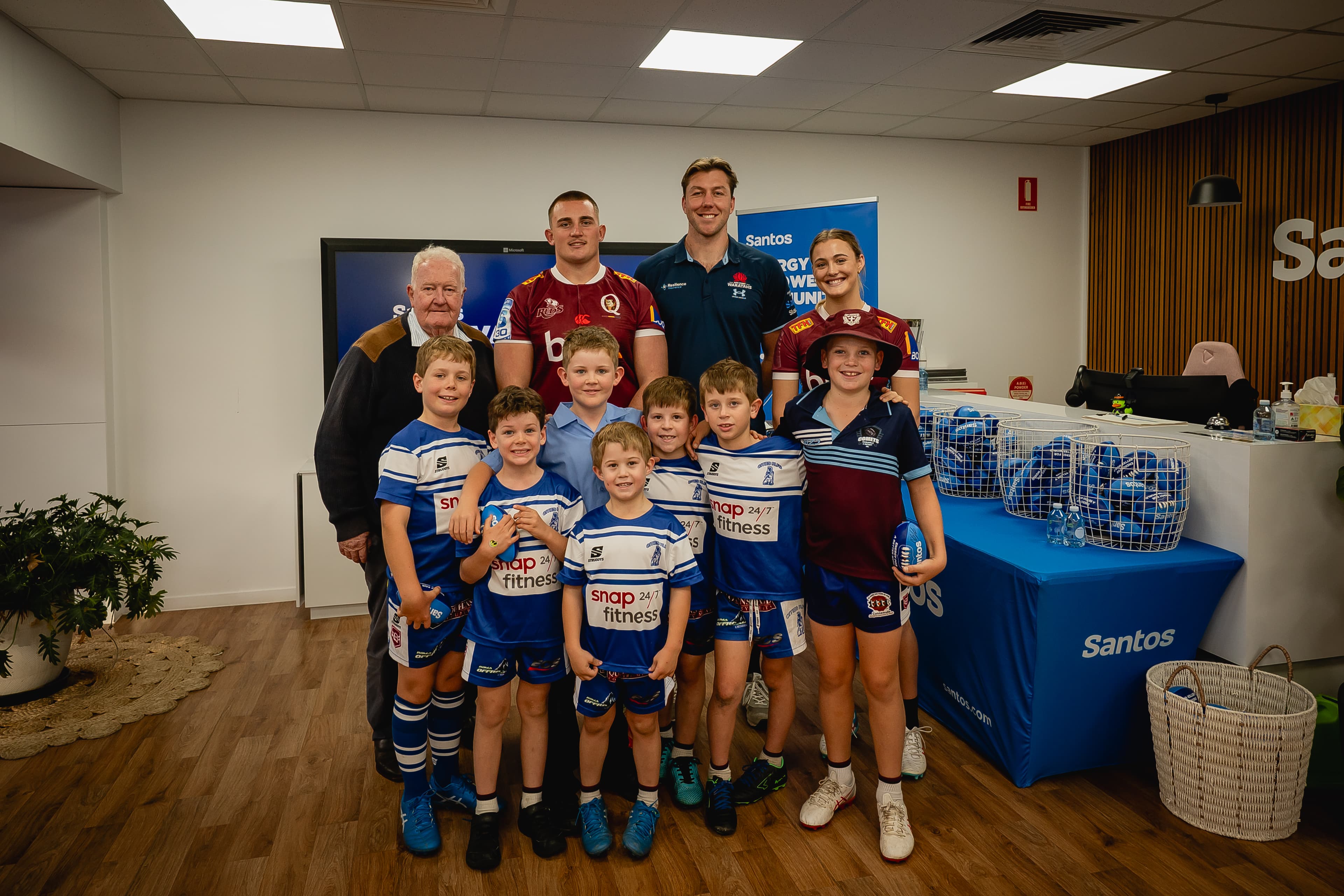 All smiles of support for the 2026 Santos Festival of Rugby...(from left) Councillor Peter Flynn, Maranoa Regional Council, Queensland Reds squad prop Kingsley Uys, NSW Waratahs lock Angus Blyth and Reds sevens player Zoe Waters and Roma rugby juniors at the Santos office in Roma